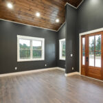 Unfurnished great room with a vaulted tongue-and-groove wood ceiling, dark walls, wood flooring, and a wood and glass front entry door