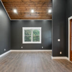 Unfurnished great room corner showing the vaulted tongue-and-groove ceiling, a single window, and the wood and glass entry door to the outside