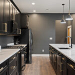 Kitchen counter with black cabinetry, gold hardware, quartz countertops, a gas cooktop, and a stainless refrigerator