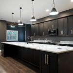 Kitchen with a long quartz-topped black island, pendant lighting, gas range, and a window overlooking trees