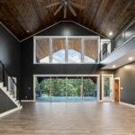 Two-story great room with vaulted tongue-and-groove wood ceiling, oversized wood ceiling fan, a wall of upper and lower windows, and a cable-railing catwalk and staircase