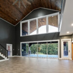 Great room with vaulted tongue-and-groove ceiling, large ceiling fan, two-story windows, and glass sliding doors leading to a covered porch