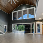 Great room with vaulted tongue-and-groove ceiling, large ceiling fan, two-story windows, and glass sliding doors leading to a covered porch