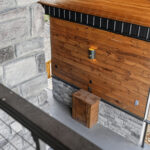 Close-up of a tongue-and-groove wood accent wall above stone wainscoting on the back porch, with a wall sconce light and a small wood storage box