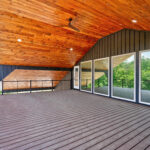 Wide covered upper deck with a wood ceiling fan, tongue-and-groove ceiling, composite decking, cable railing, and large windows looking into an interior room