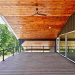 Vertical view of the covered upper deck's tongue-and-groove wood ceiling and fan, with composite decking, cable railing, and glass doors leading into the house
