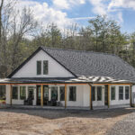 Aerial view of The Ridgeview farmhouse home with wraparound porch and board-and-batten siding on wooded land in Crossville, TN