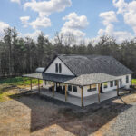 Aerial angle view of the farmhouse home showing the gable roofline and surrounding tree line