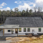 Rear aerial view of the farmhouse home showing the second-story gable window and back deck