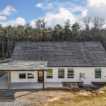 Front approach view of the farmhouse home with covered wraparound porch and gravel driveway
