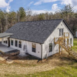 Rear aerial view of the farmhouse home showing the second-story gable window and back deck