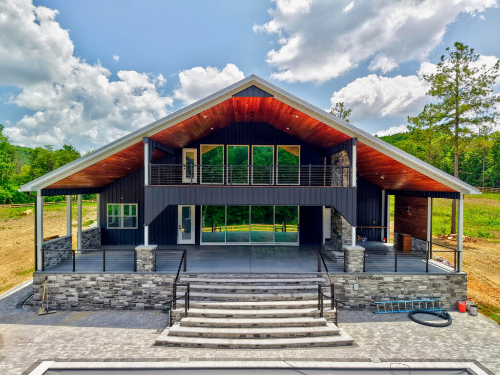 Close aerial view of the home's rear porch with a wood-planked vaulted ceiling, stone columns, glass sliding doors, and an upper-level deck