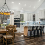 Open kitchen with white cabinetry, blue subway tile backsplash, and a large island with black stools
