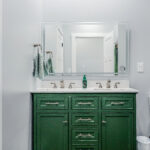 Guest bathroom with a green vanity, double sinks, and a backlit mirror