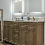 Primary bathroom with a double vanity, marble-look countertop, and backlit mirrors