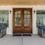 Wood and glass double front door flanked by wicker chairs on the covered porch
