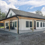 Completed exterior of the farmhouse home with wraparound porch, board-and-batten siding, and gravel driveway