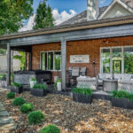 Exterior view of the completed outdoor living space with motorized screens open, hot tub, and seating beneath the standing seam roof