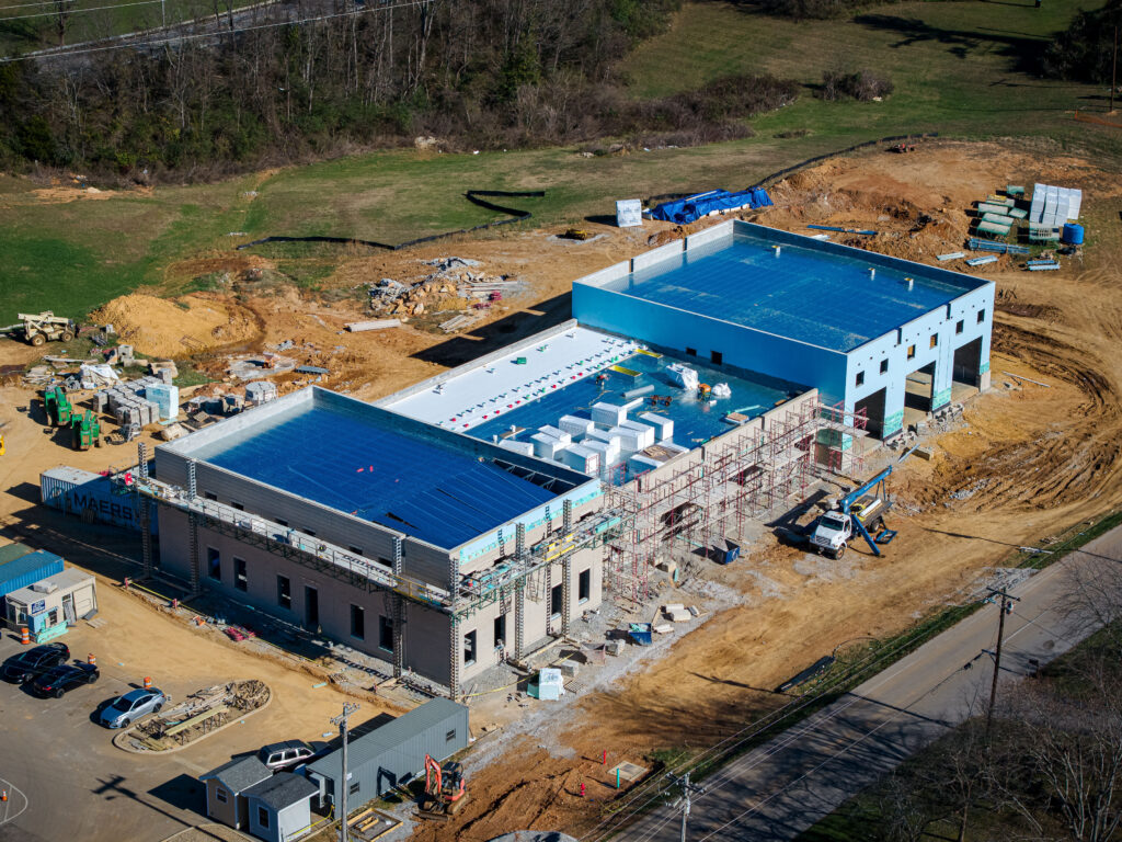 Three quarter aerial of the TCAT Livingston structural steel building with metal roof decking across both end sections and scaffolding along the center bay